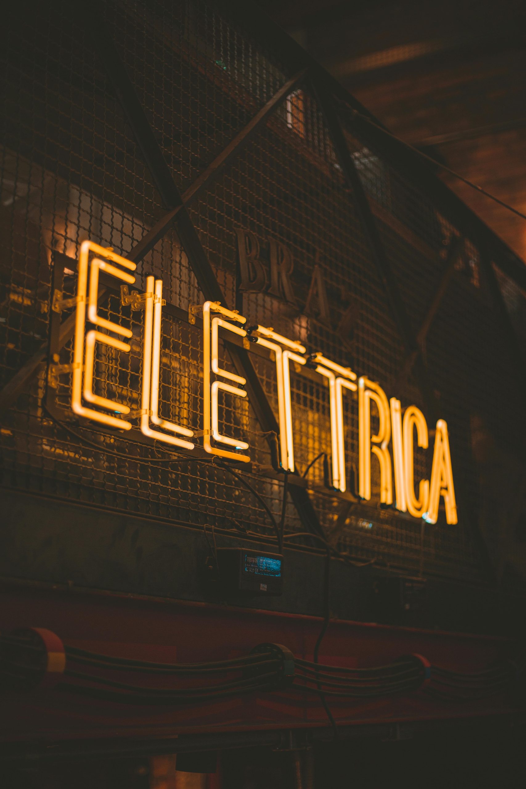 Moody urban photo of an illuminated 'Elettrica' neon sign in warm tones.