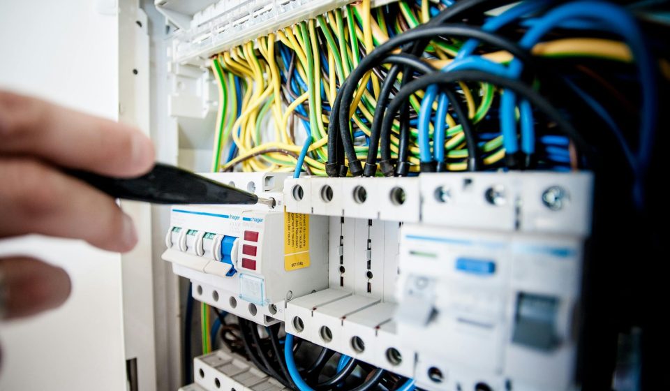 Hand of electrician working on a circuit breaker panel with colorful wires, ensuring safe electrical connections.
