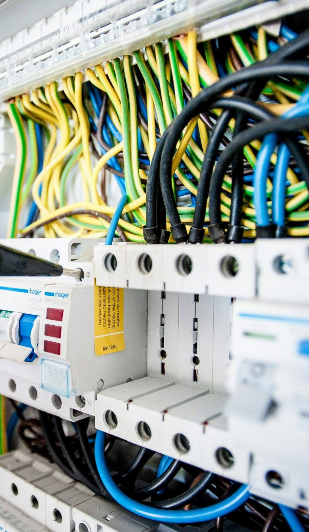 Hand of electrician working on a circuit breaker panel with colorful wires, ensuring safe electrical connections.